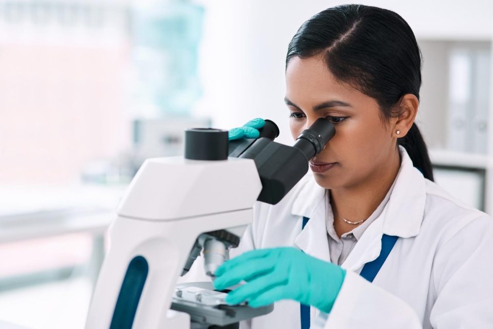 Scientist in lab looking through microscope